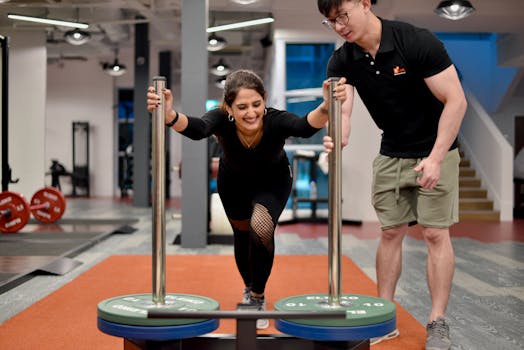 Asian female athlete pushing prowler sled under trainer's guidance in Singapore gym.
