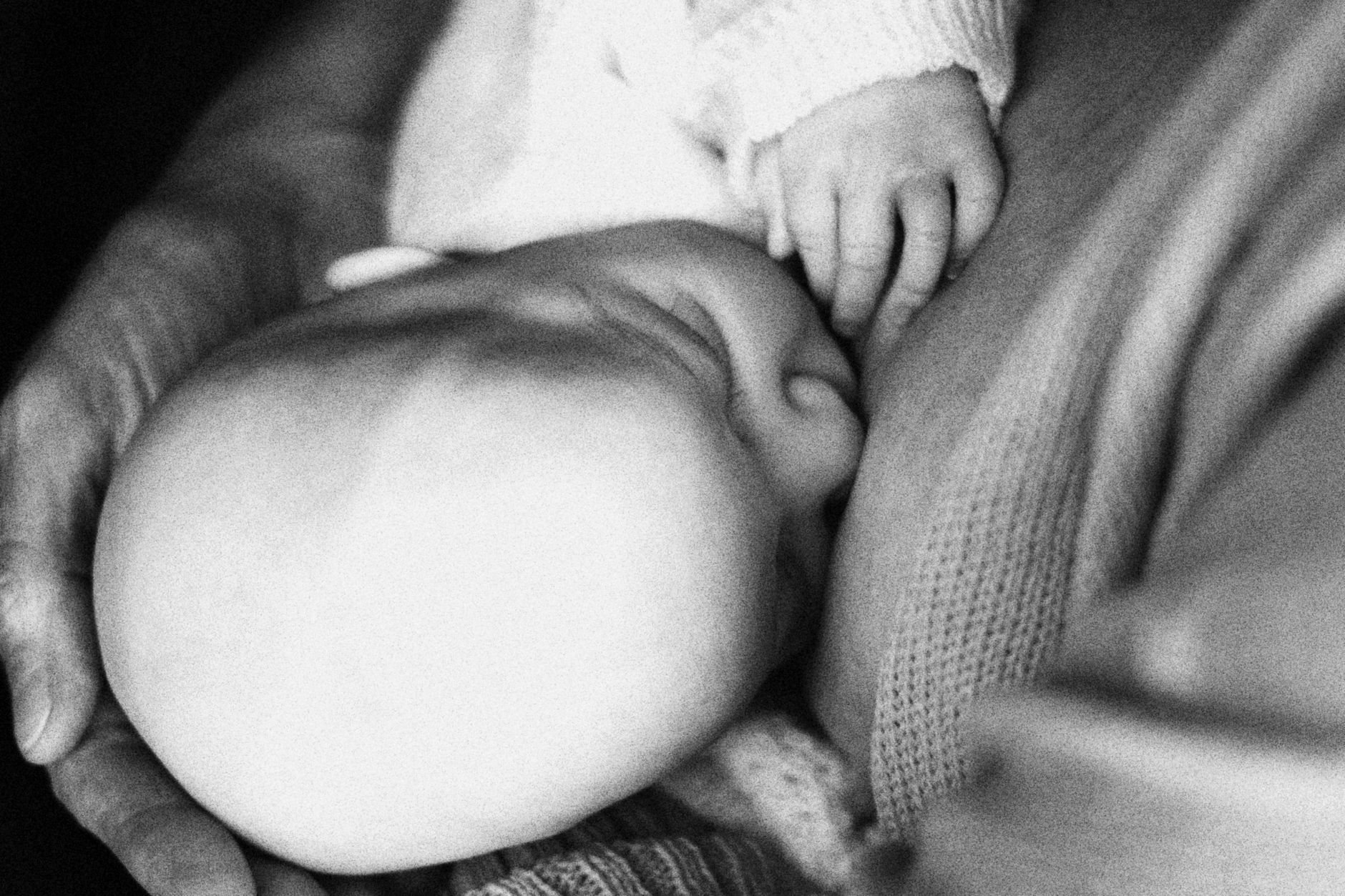 Tender black and white photograph capturing a close-up moment of a newborn cradled in a loving hand.