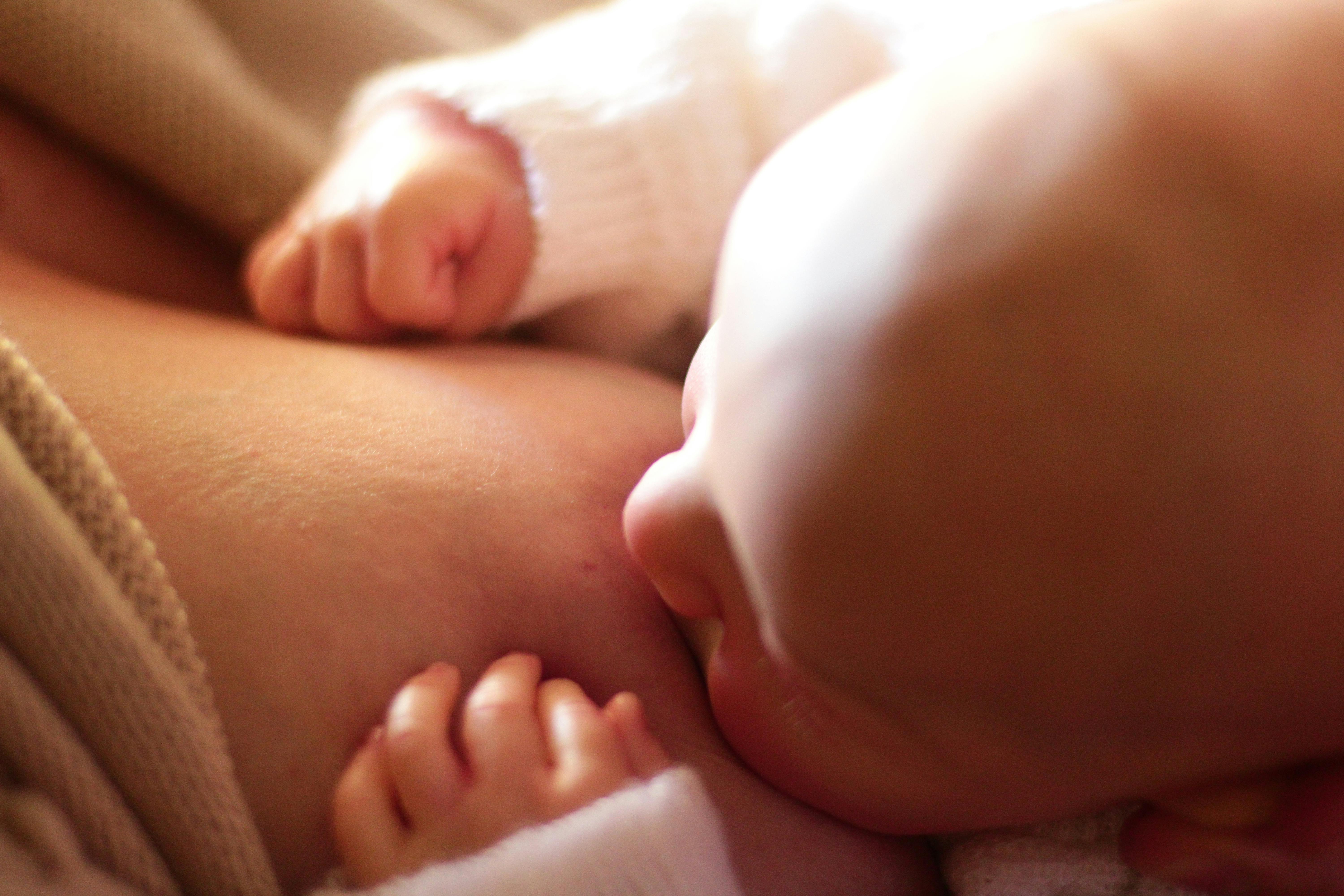 Intimate close-up of a newborn baby breastfeeding, captured in warm, softly lit setting.
