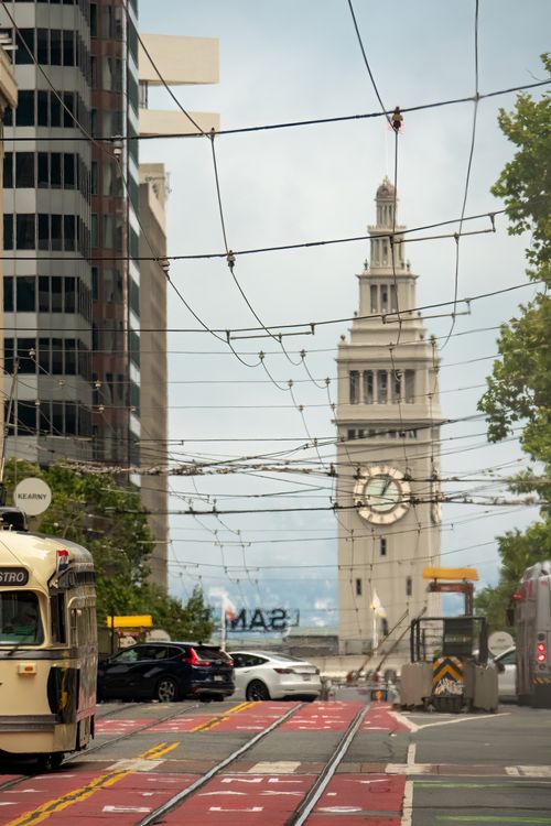 Free View of San Francisco's iconic Ferry Building clock tower through a busy downtown street with streetcars and city traffic. Stock Photo