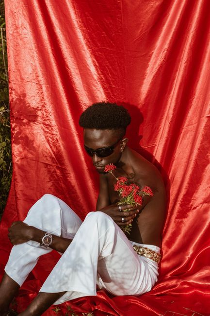 Fashionable man in sunglasses holding flowers against a vibrant red backdrop. Trendy and artistic.