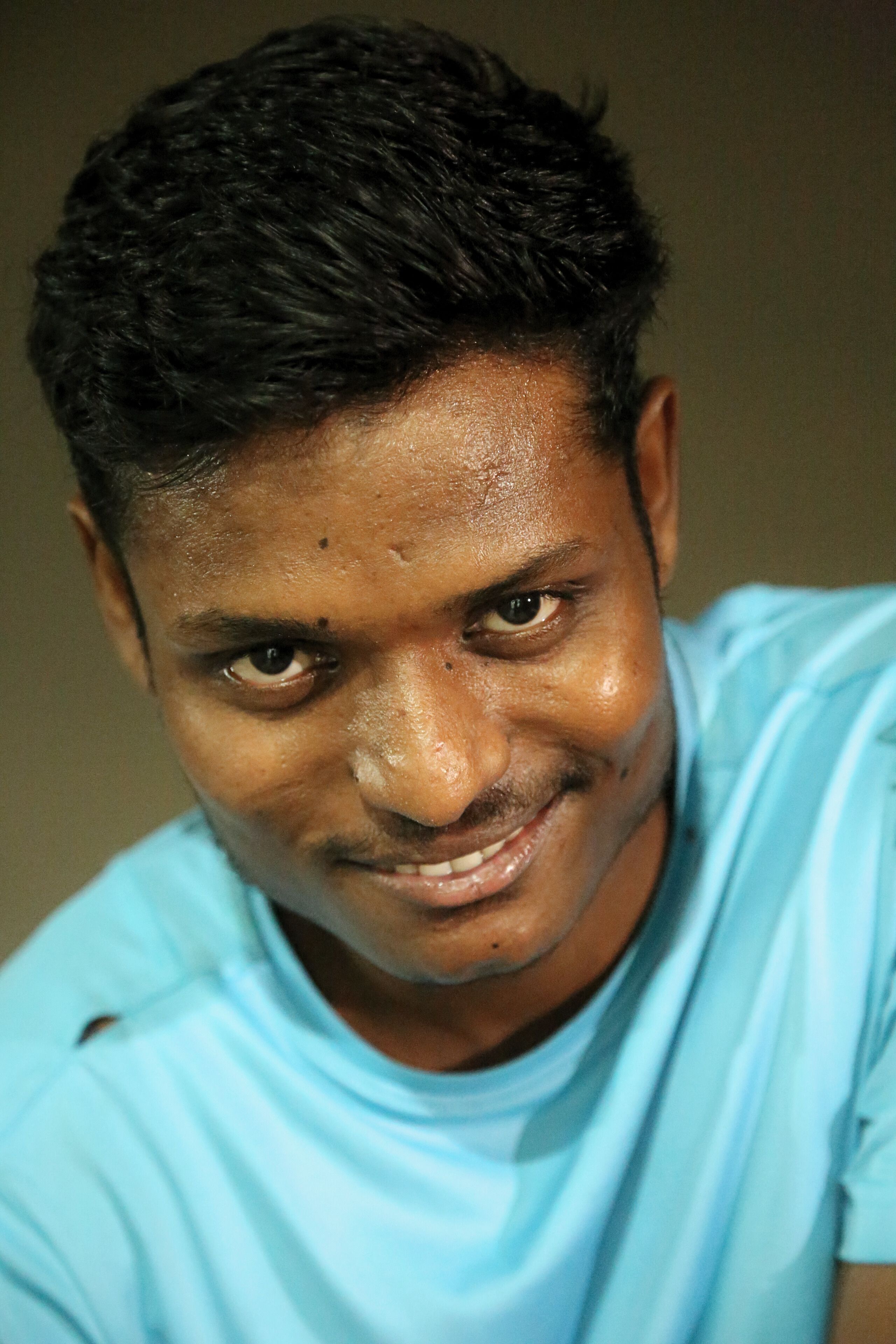 Close-up portrait of a smiling young man in a blue t-shirt in Jhusi, India.
