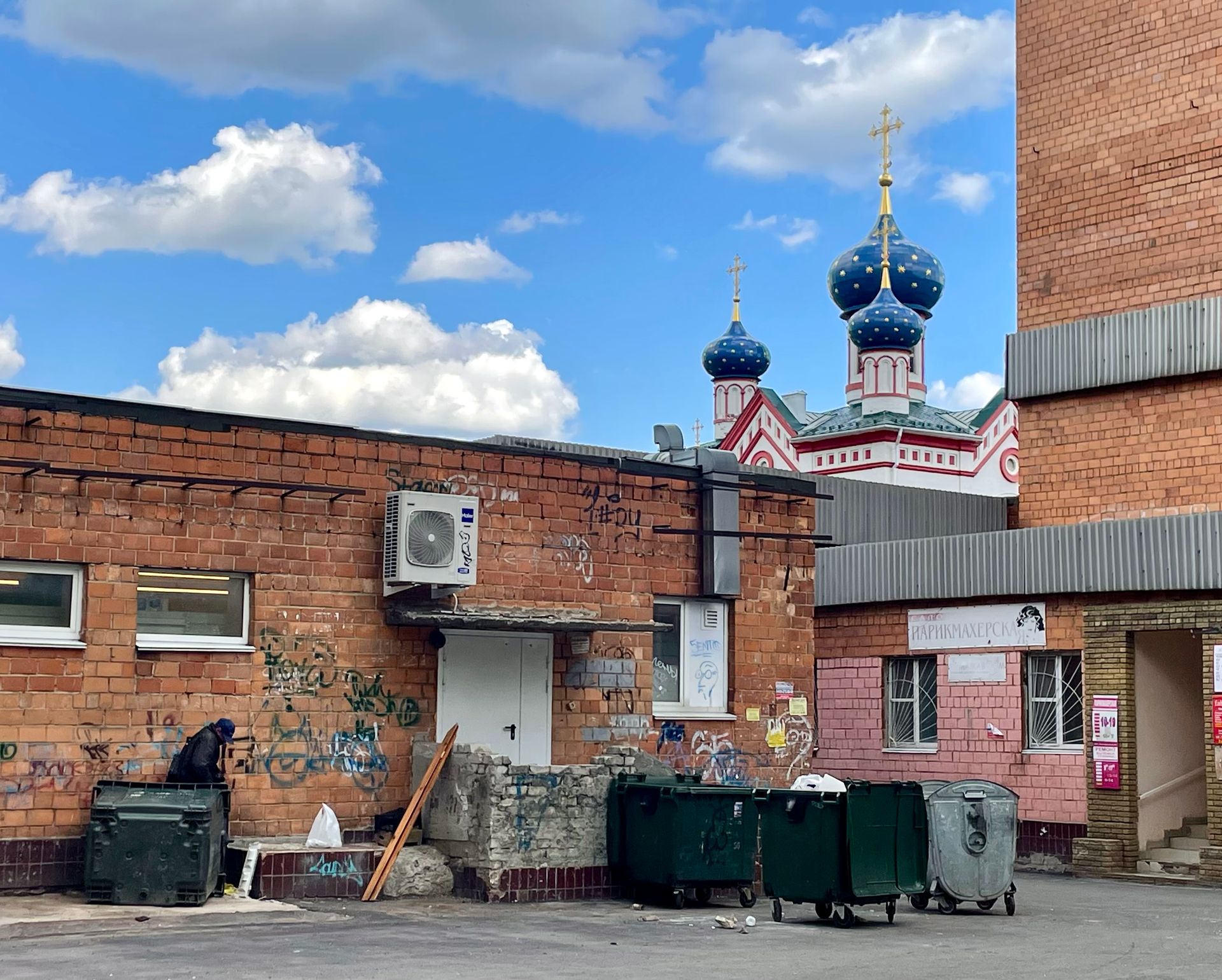 Urban scene with graffiti walls and a distant Russian Orthodox Church under a blue sky.