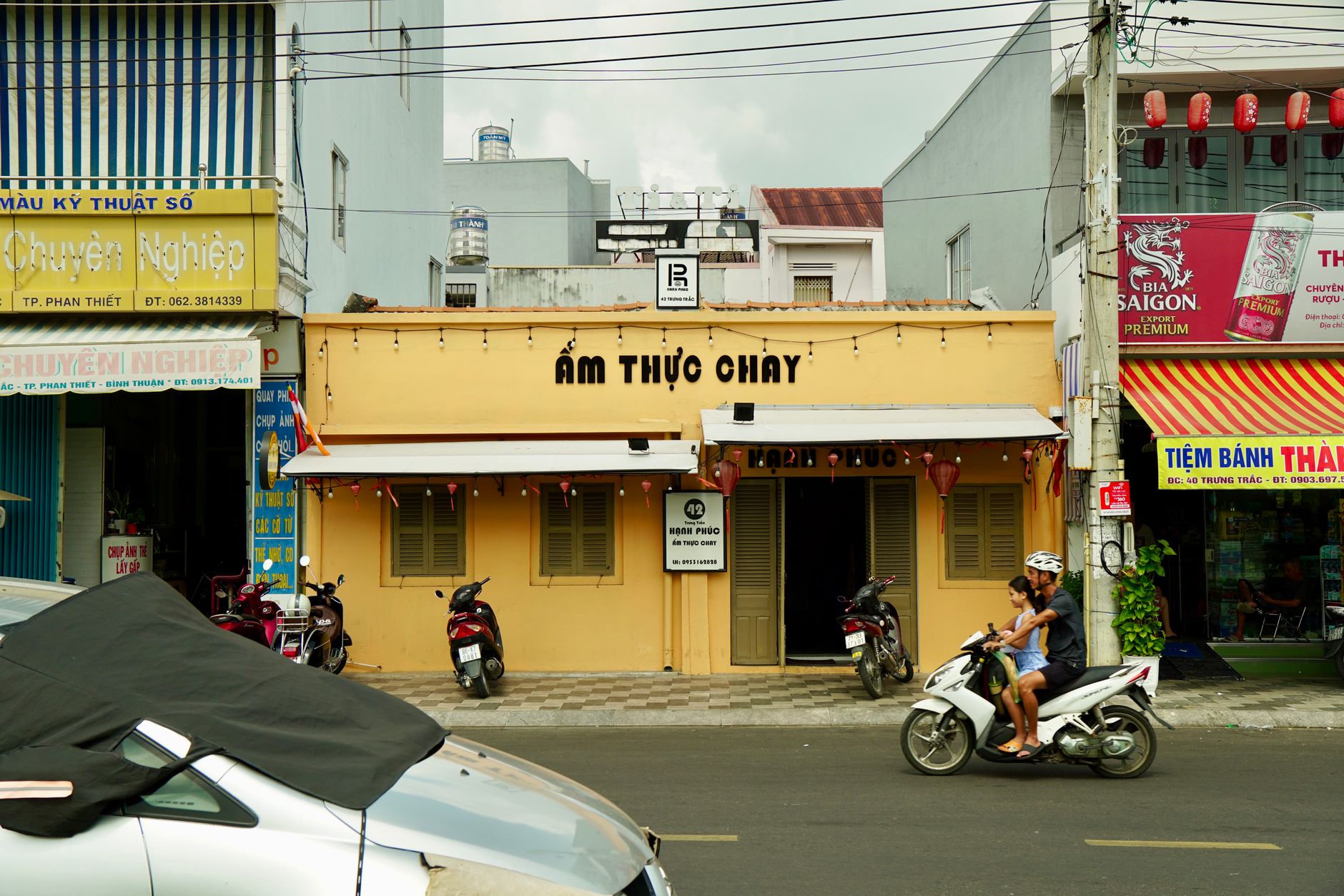 Street scene in Vietnam featuring a restaurant and passing motorbikes, capturing local urban life.