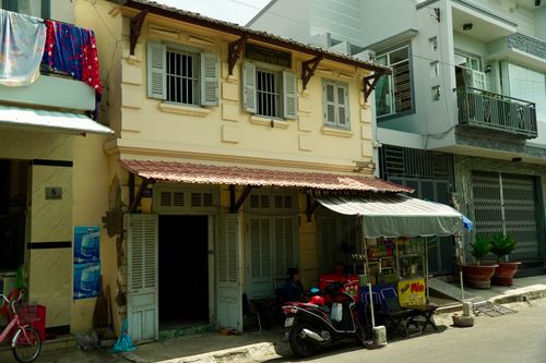 Free A quaint Vietnamese street scene featuring traditional architecture and a local shop under a sunny sky. Stock Photo