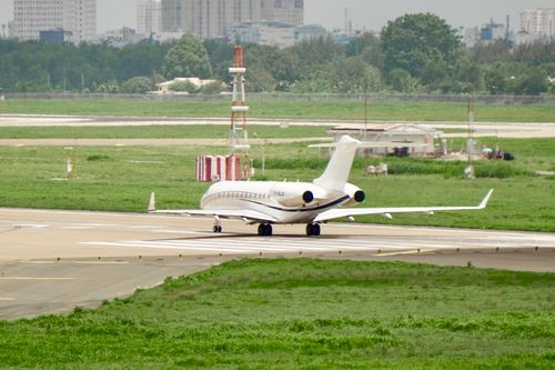 Free A sleek private jet taxiing on a runway at an international airport, with city skyline in the background. Stock Photo