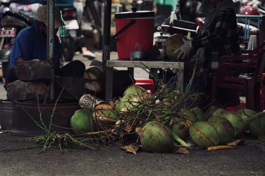 Street vendor preparing fresh coconuts at an outdoor market with vibrant display.