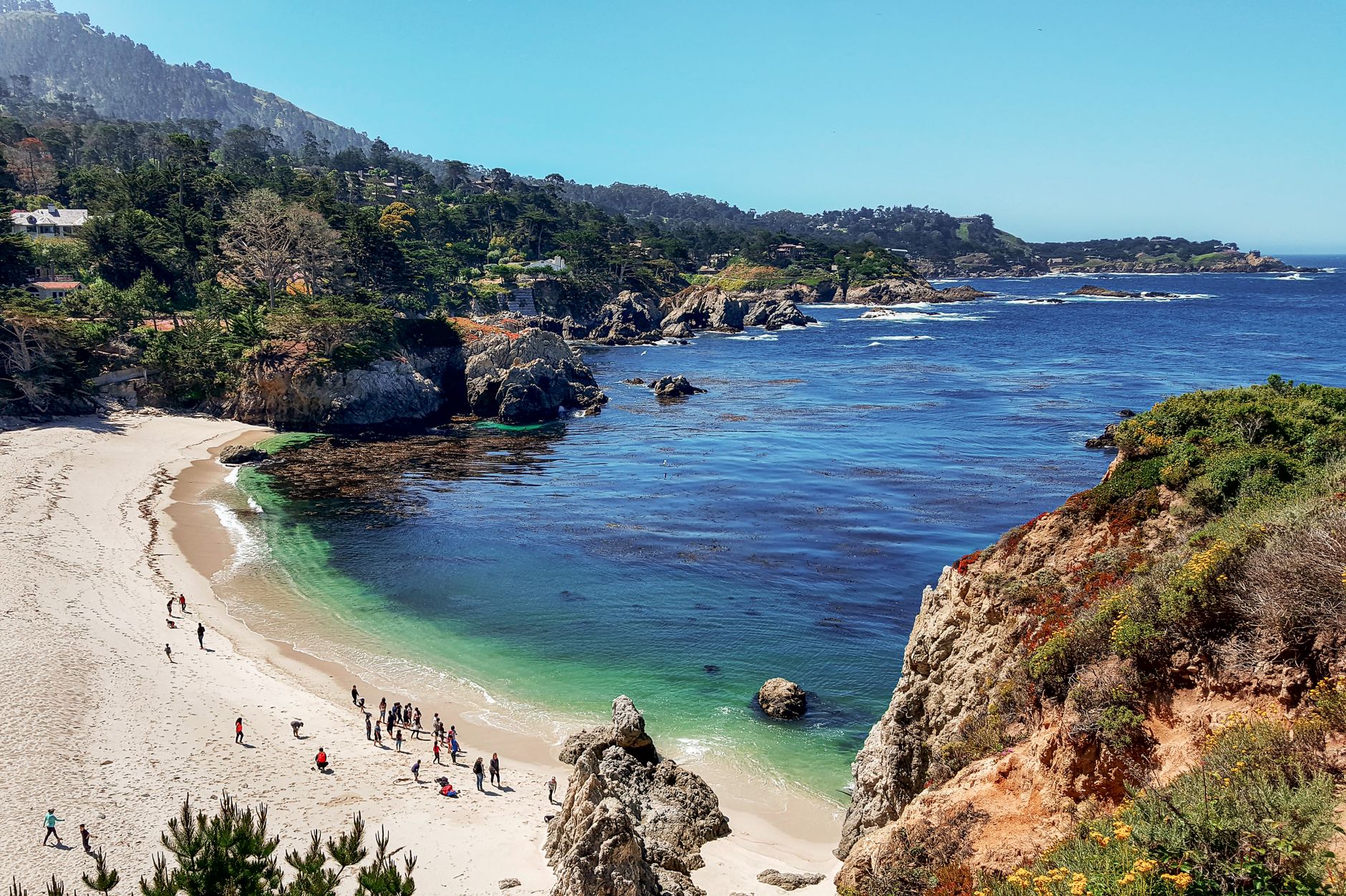 A picturesque view of the coastline with people enjoying the beach at Carmel-by-the-Sea, California.
