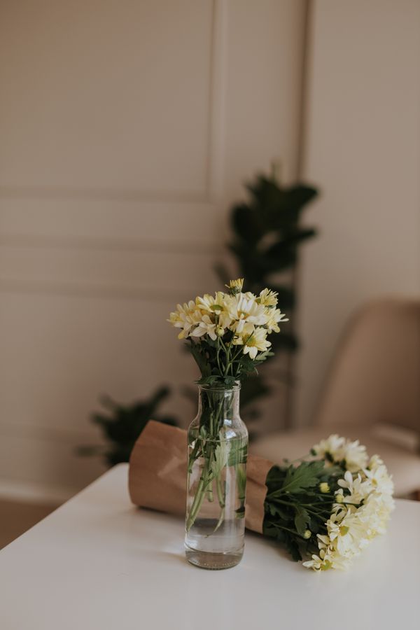 Ambiente interno chique com flores brancas e amarelas em um vaso de vidro com iluminação suave.