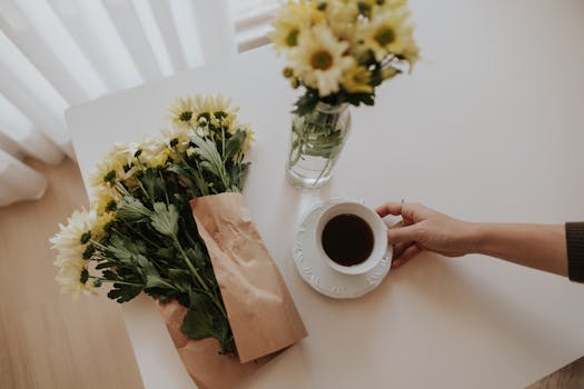 Flat lay of morning coffee with yellow daisies on a white table, creating a calming atmosphere.