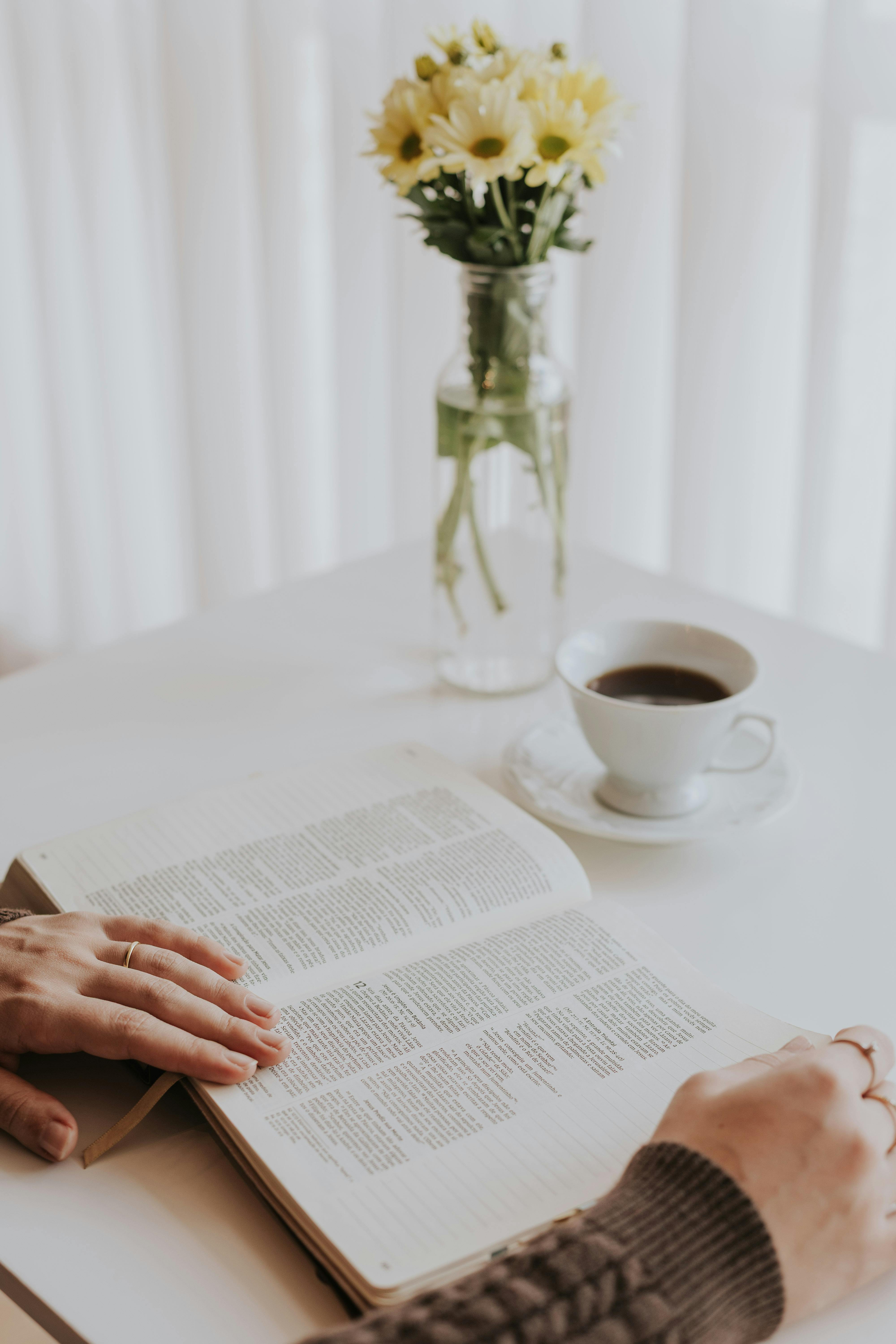 A tranquil morning scene with a book, coffee, and vase of flowers on a table.