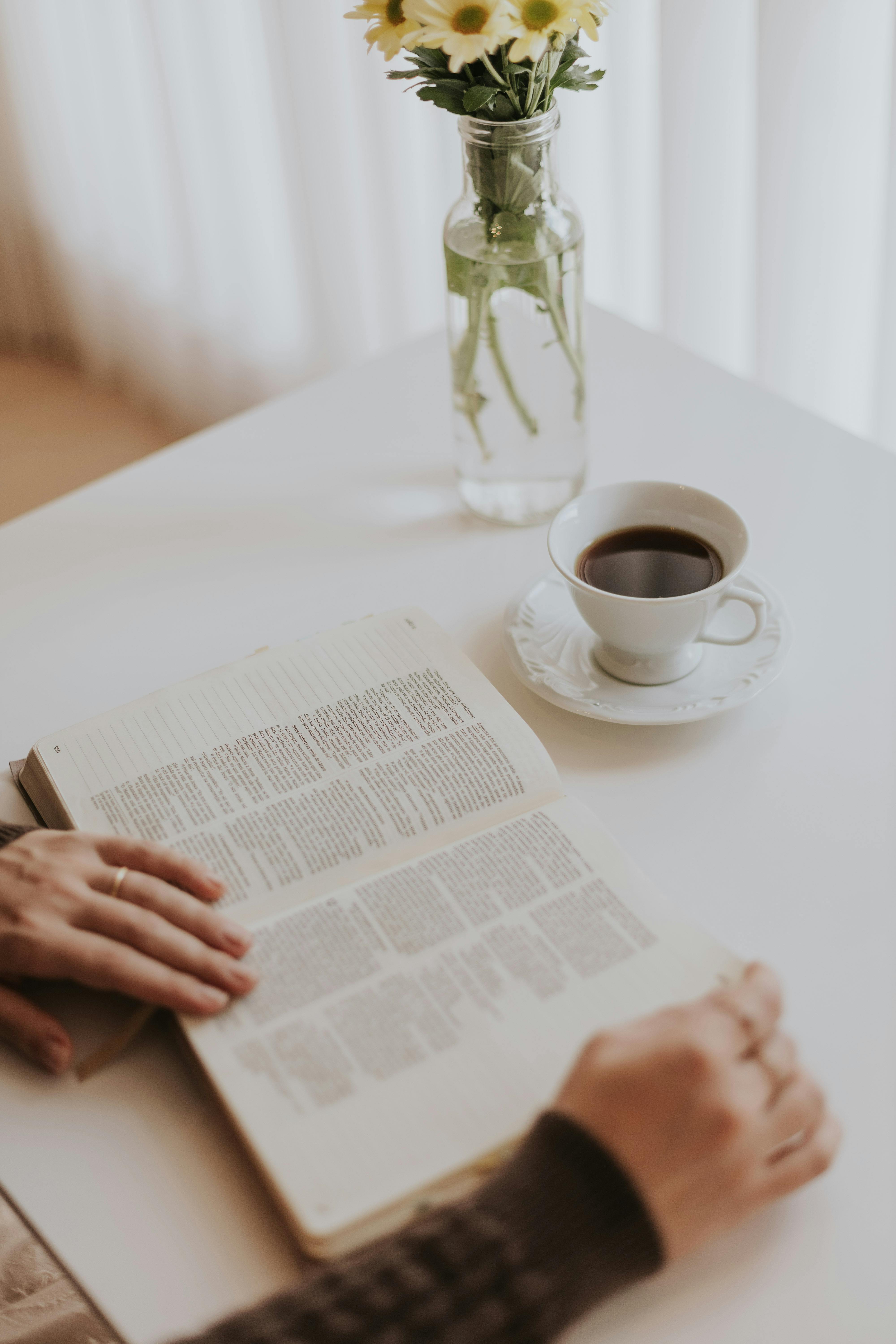 A peaceful morning scene featuring a person reading a book with flowers and a coffee cup.