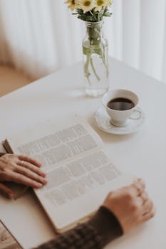 A peaceful morning scene featuring a person reading a book with flowers and a coffee cup.