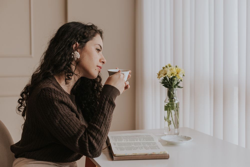 A woman relaxing with a cup of tea and a book by a bright window