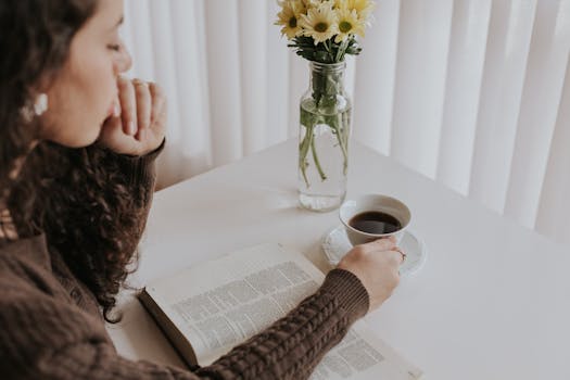 Woman enjoying a peaceful moment with a book and coffee at a table adorned with flowers.