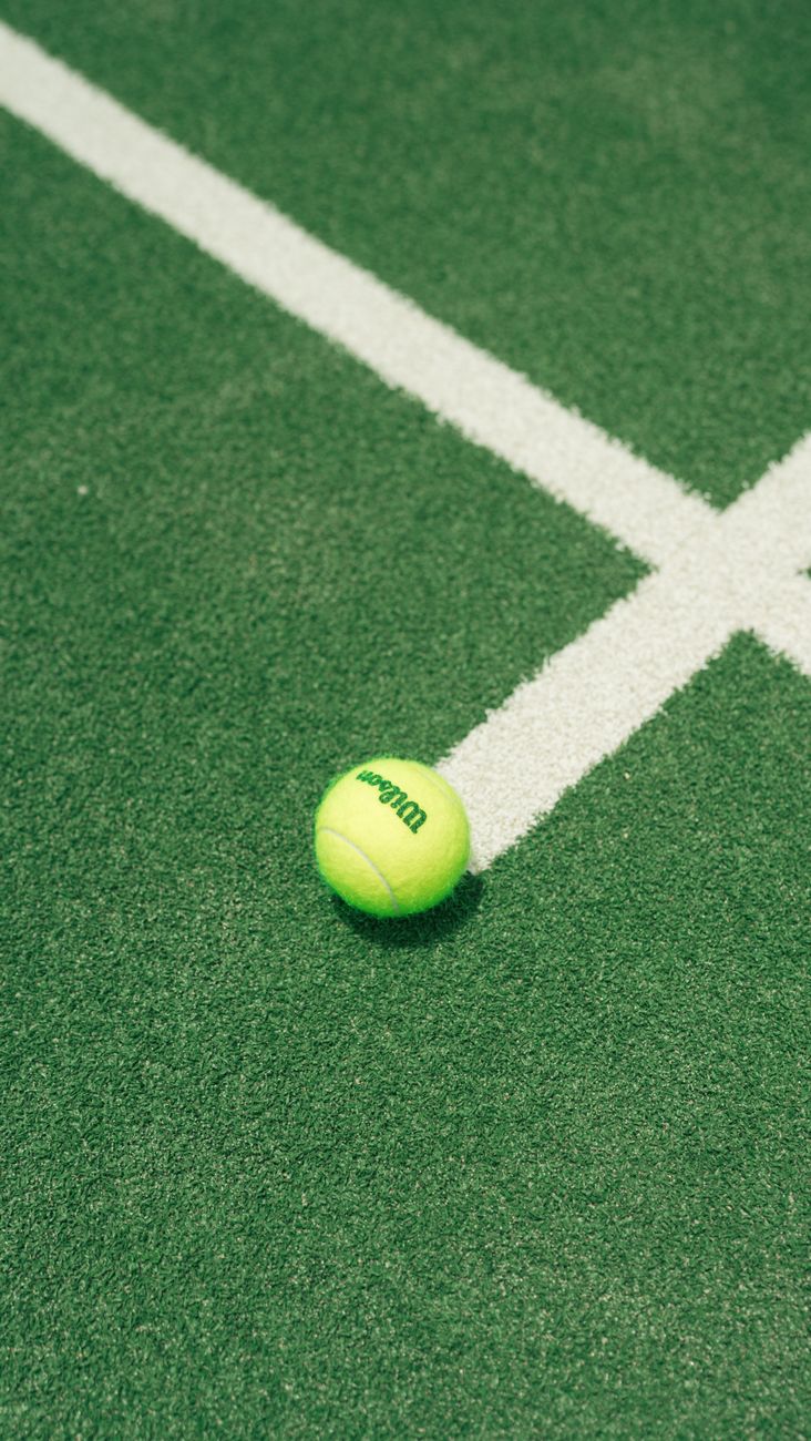Close-up van een tennisbal op een groene baan met witte lijnen, thema buitensporten.