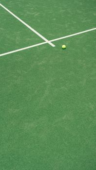 Vibrant green tennis court surface with a tennis ball near white lines, perfect for sports themes.