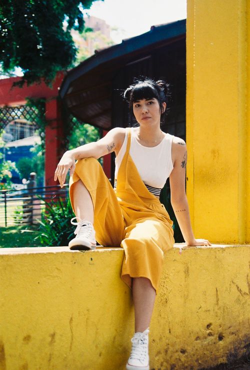Free Young woman in a yellow jumpsuit relaxing outdoors in a vibrant setting, captured in Paraná, Brazil. Stock Photo