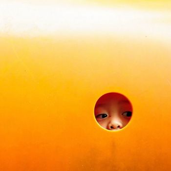 A child peeks through a circular hole in vibrant orange playground equipment.