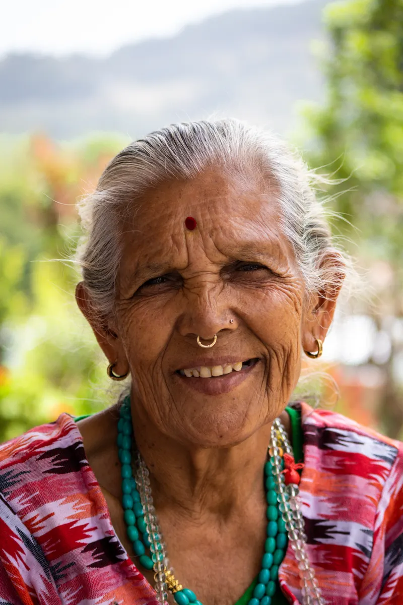 A smiling older woman in a saree outdoors in the late afternoon