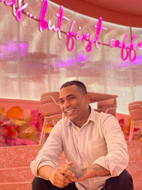 Free A cheerful man sits in a colorful café with neon lights and pink decor. Stock Photo