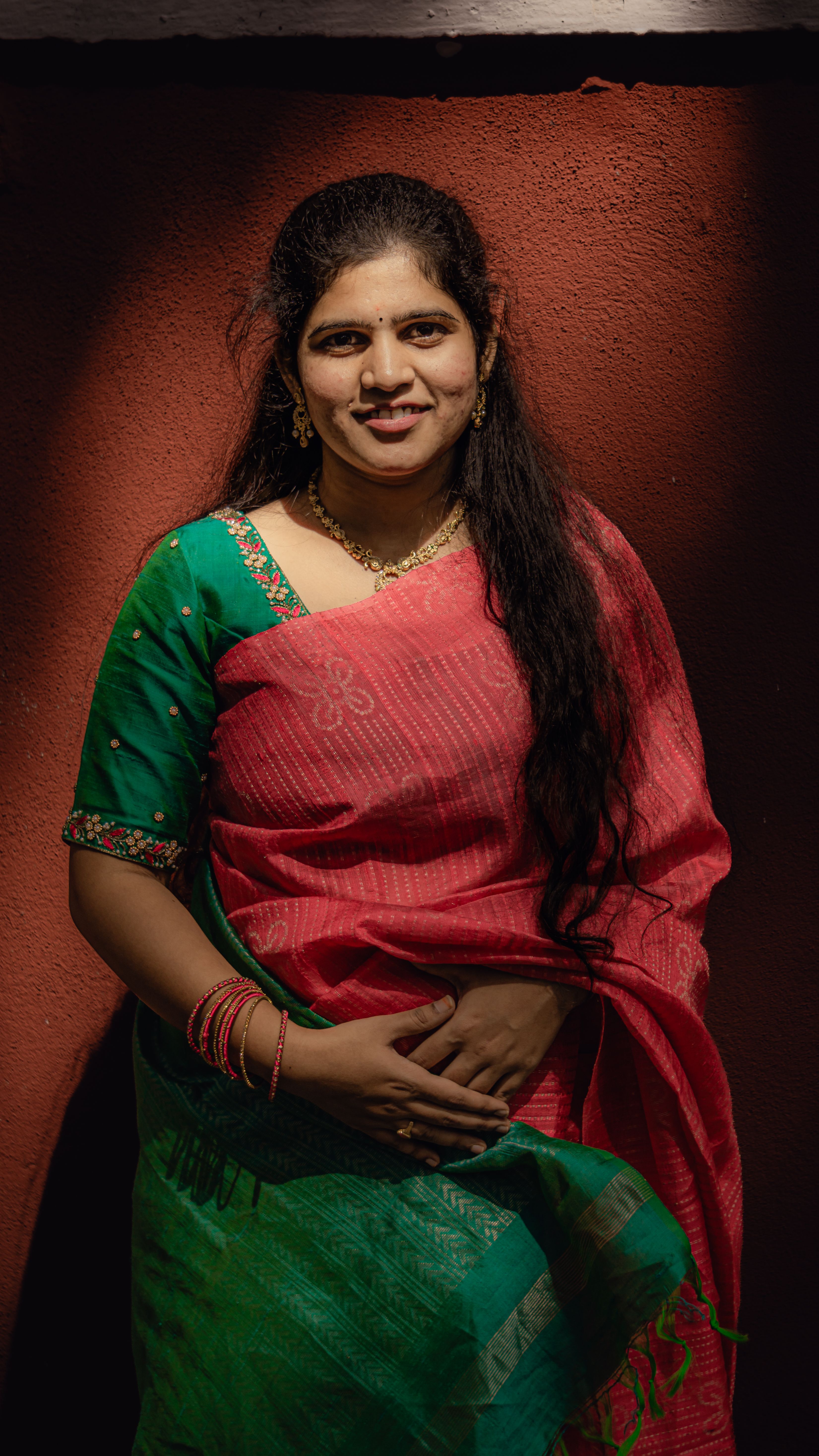 Portrait of a smiling woman in a colorful saree against a red wall, capturing natural beauty and cultural richness.