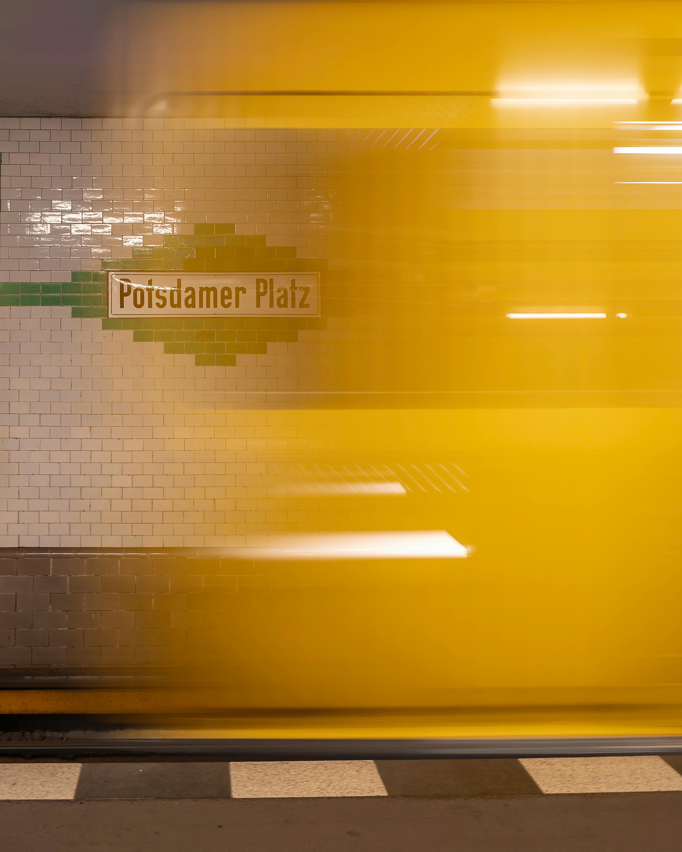 Blurred yellow train passing Potsdamer Platz station sign in Berlin subway.