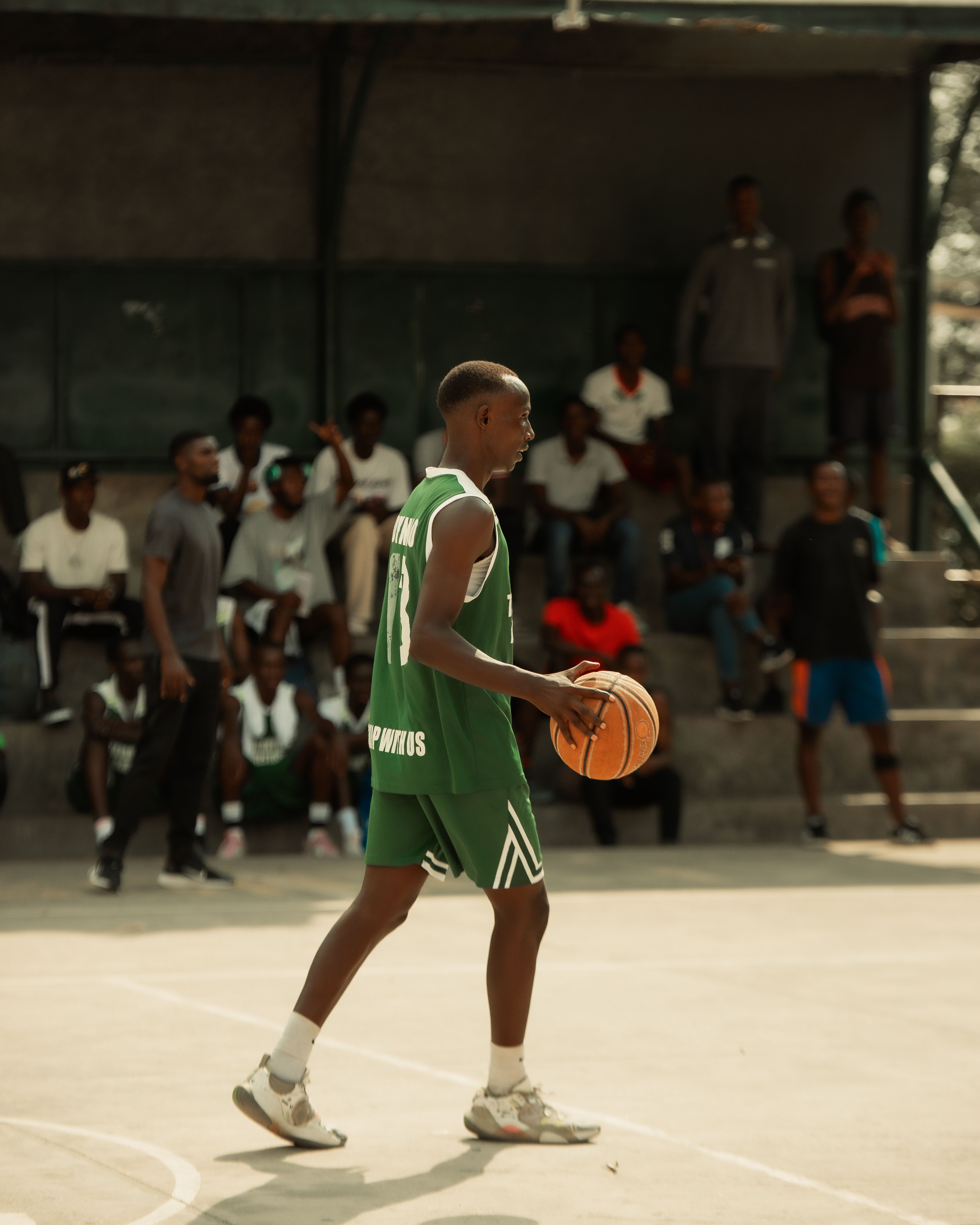 A basketball player dribbles on an outdoor court during a vibrant match with spectators.