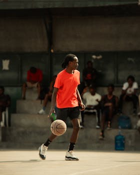 A young man skillfully dribbles a basketball on an outdoor court with people watching.