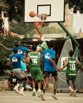 Dynamic street basketball game with players making a jump shot outdoors.