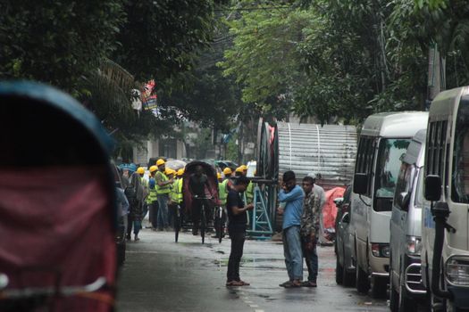 City street with construction workers, rickshaws, and parked vans in a busy urban area.