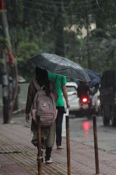 Person walking on a wet street under an umbrella during a rainy day, capturing urban life.