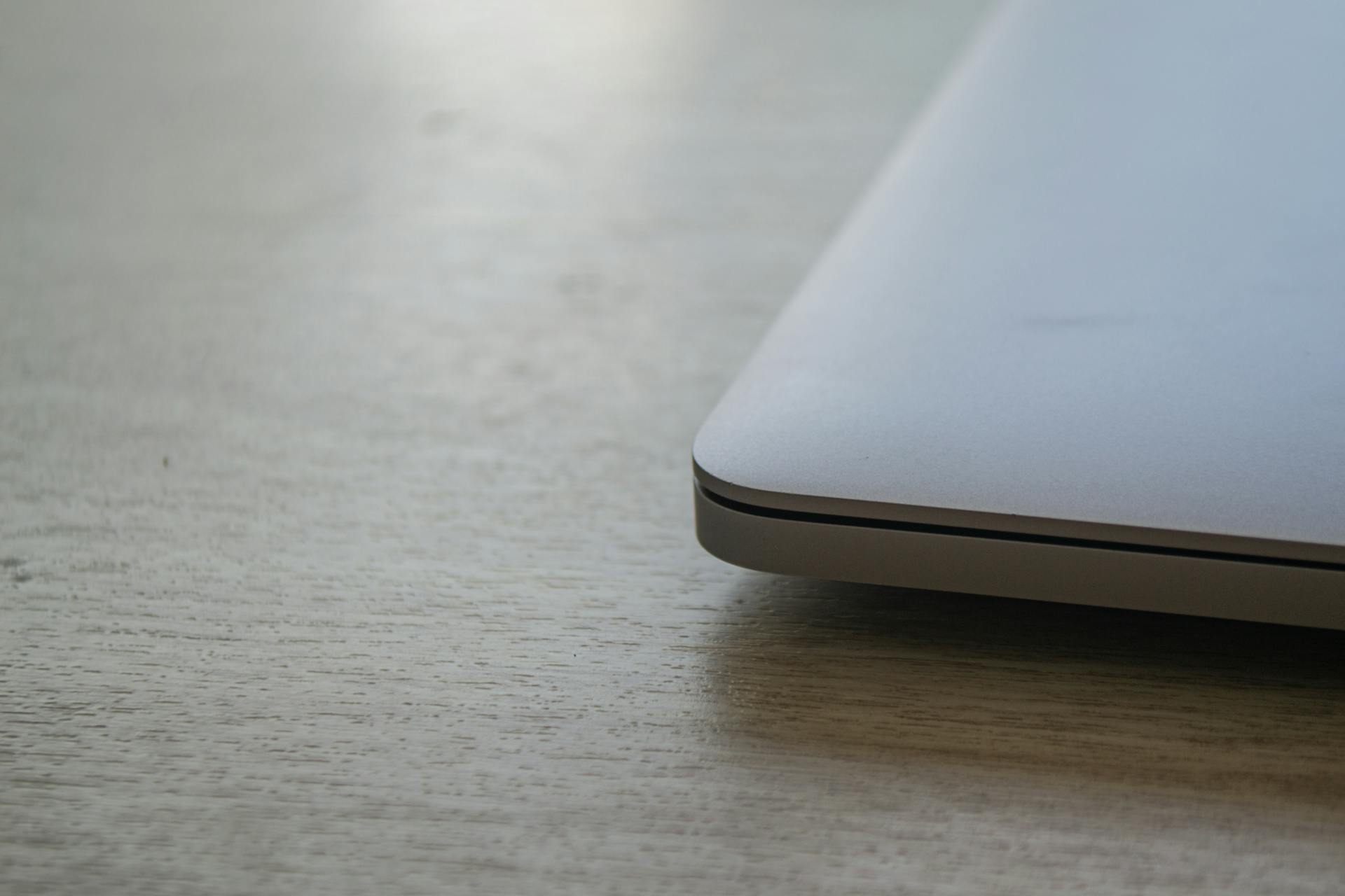 Close up of a sleek modern laptop corner on a wooden desk surface, emphasizing minimalist design.