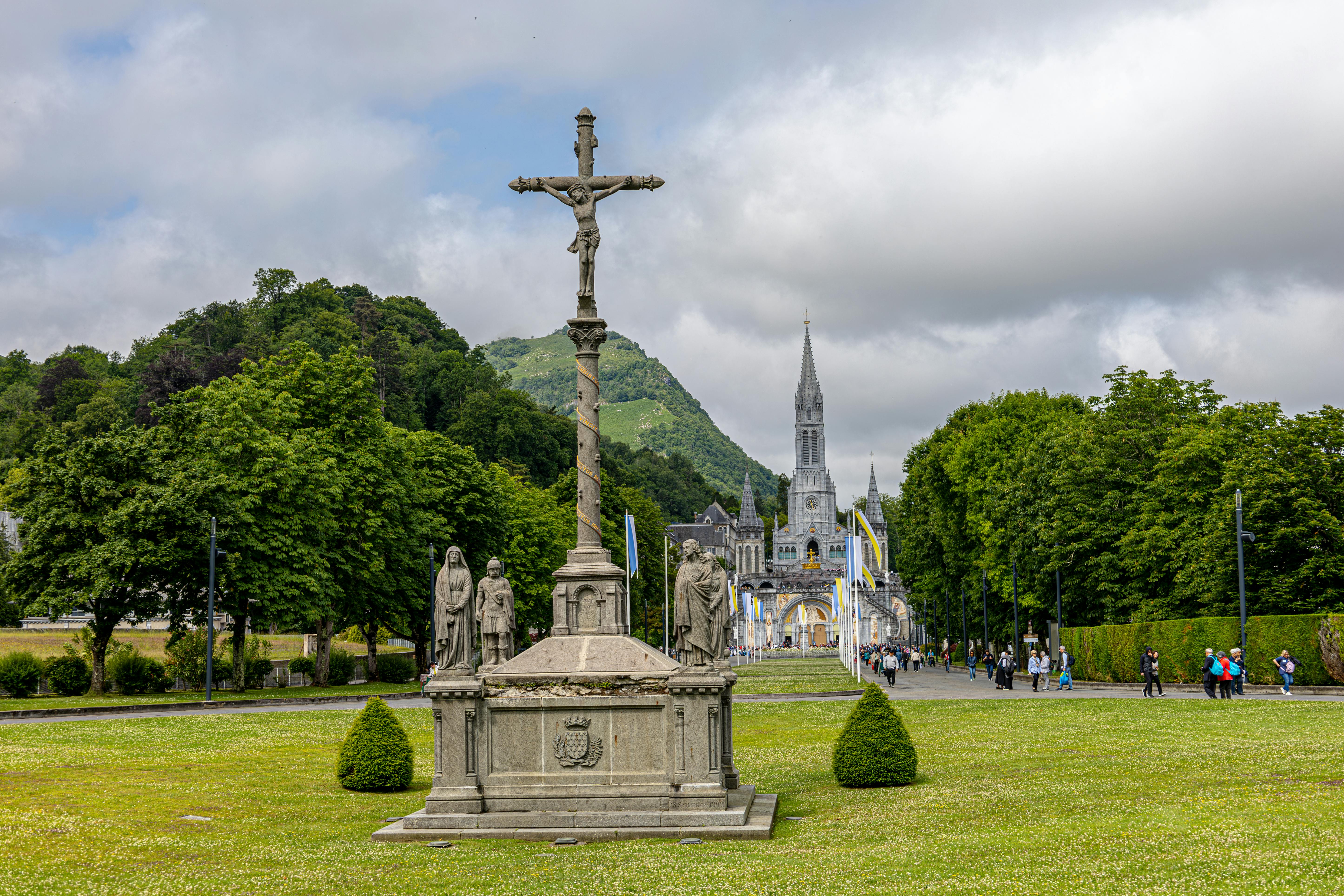 Scenic view of Lourdes Basilica with ornate cross under cloudy sky, France.