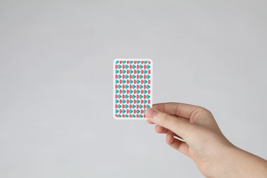 Clean minimalist image featuring a hand holding a colorful patterned playing card.