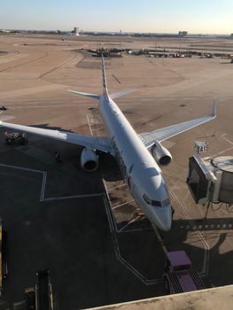 A commercial airplane parked at a gate in a busy airport under a clear sky.