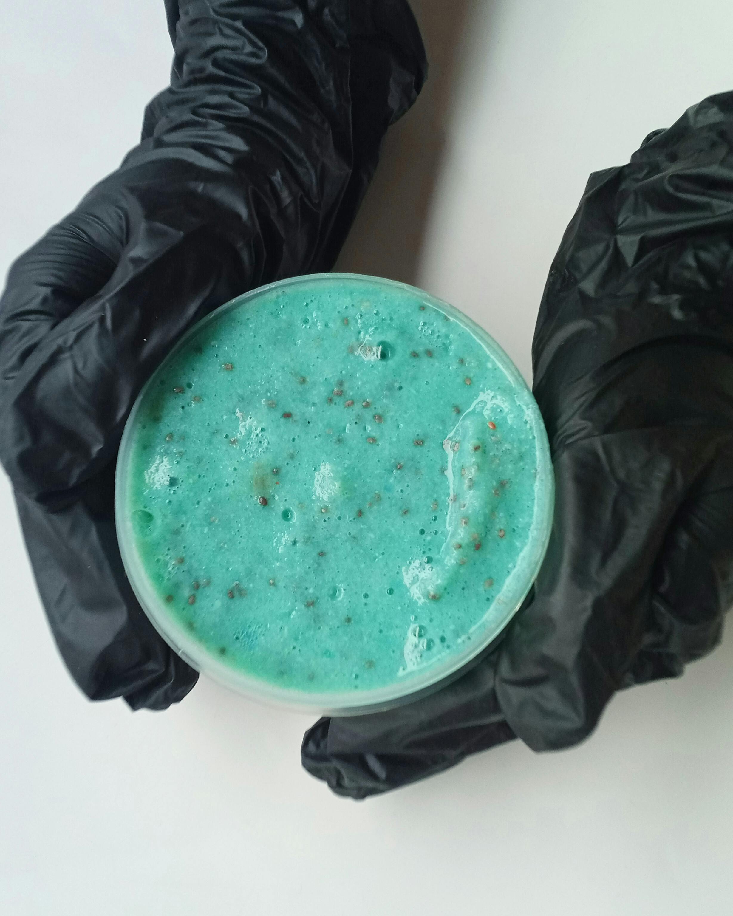 Close-up of a vibrant blue exfoliating scrub held by gloved hands on a white background.