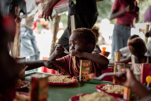 A young child relishing a meal outdoors, showcasing community and joy.