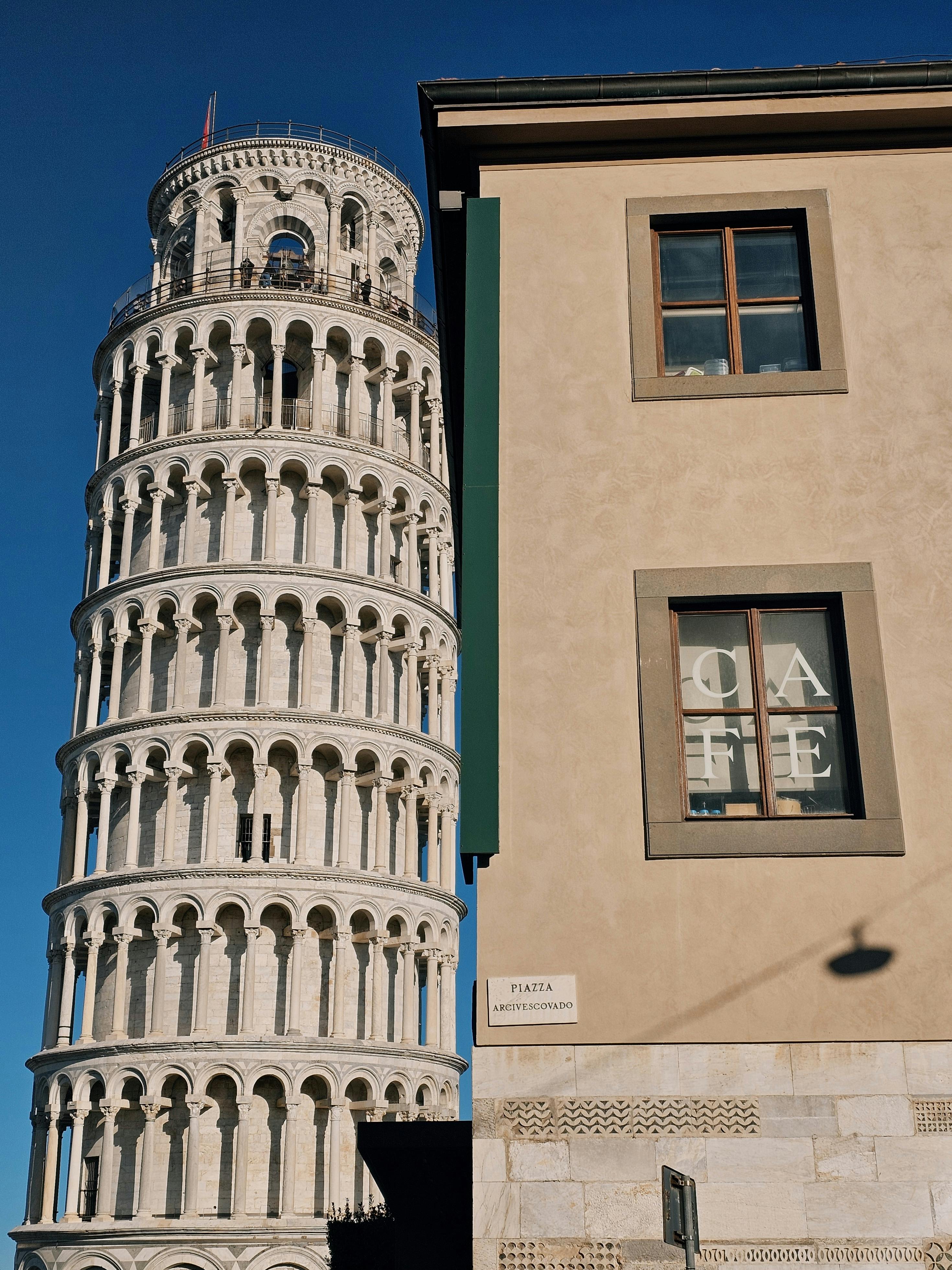 Leaning Tower of Pisa with adjoining building under a clear blue sky in Tuscany, Italy.