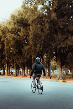 Person cycling on a road in Buenos Aires park with lush trees and warm lighting.