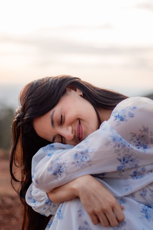 Free A woman in a floral dress smiling peacefully outdoors at sunset, embracing tranquility. Stock Photo