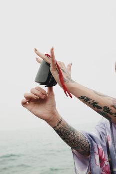 Tattooed hands skillfully playing castanets near the ocean, showcasing a mix of body art and traditional instruments.