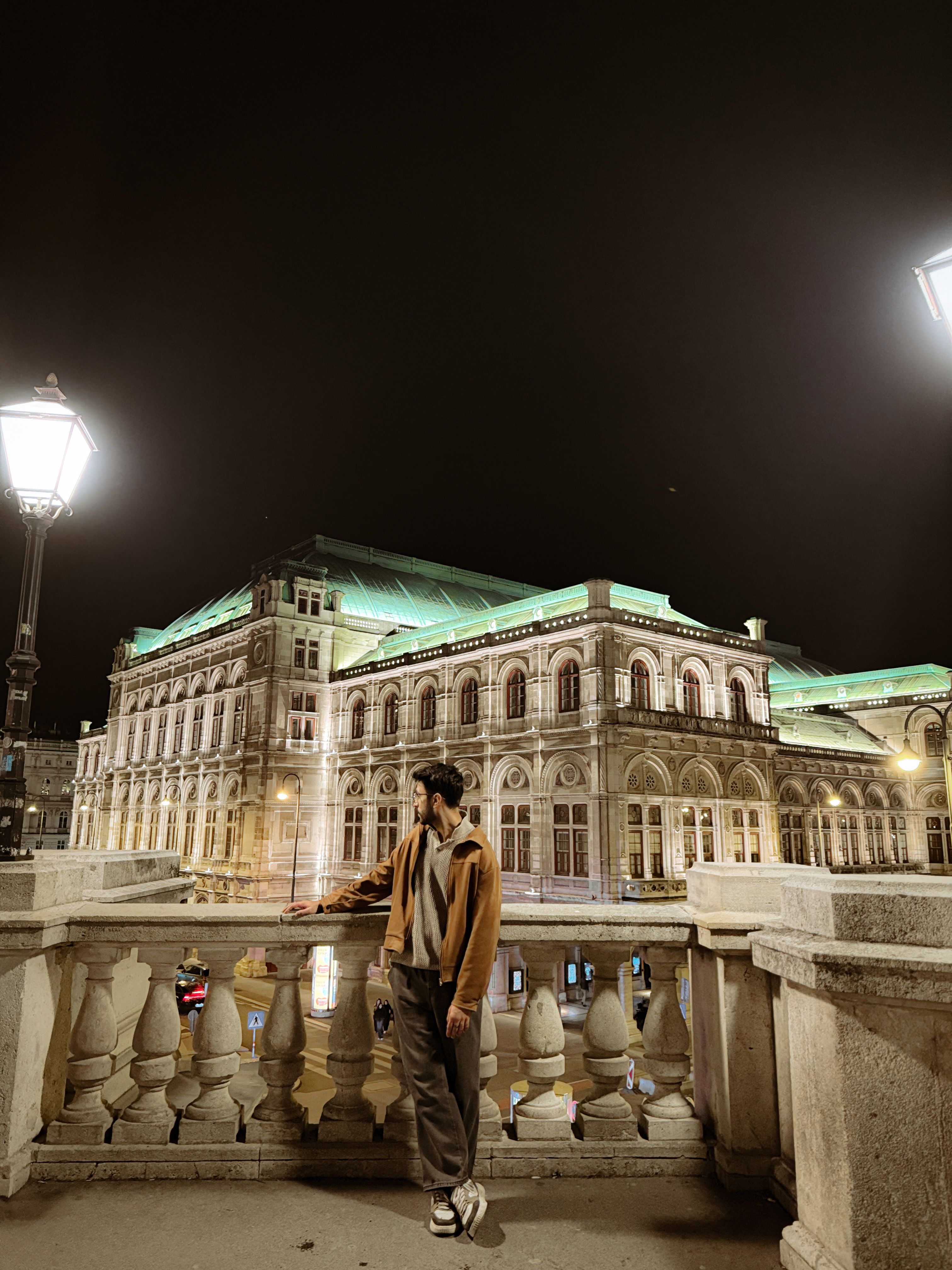 A man explores the Vienna State Opera at night, highlighting its elegant architecture.
