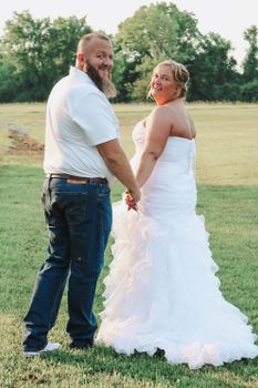 Smiling bride and groom holding hands outdoors in a sunny wedding scene.