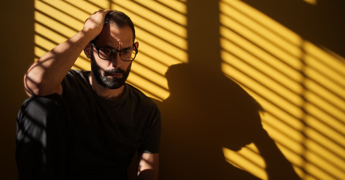 Contemplative man with dramatic shadows, moody indoor scene.