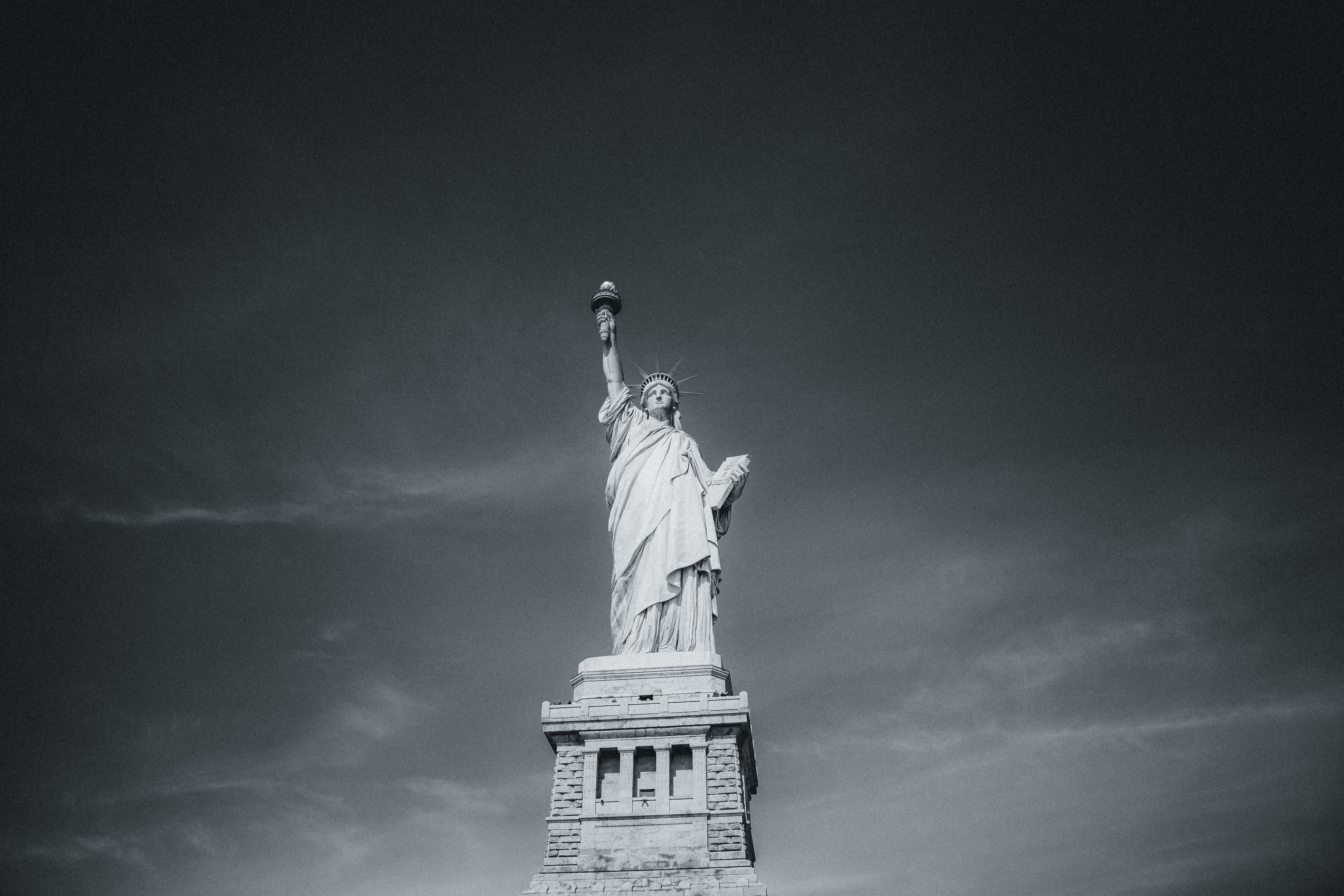 Black and white photograph of the Statue of Liberty standing tall against the sky in New York City.