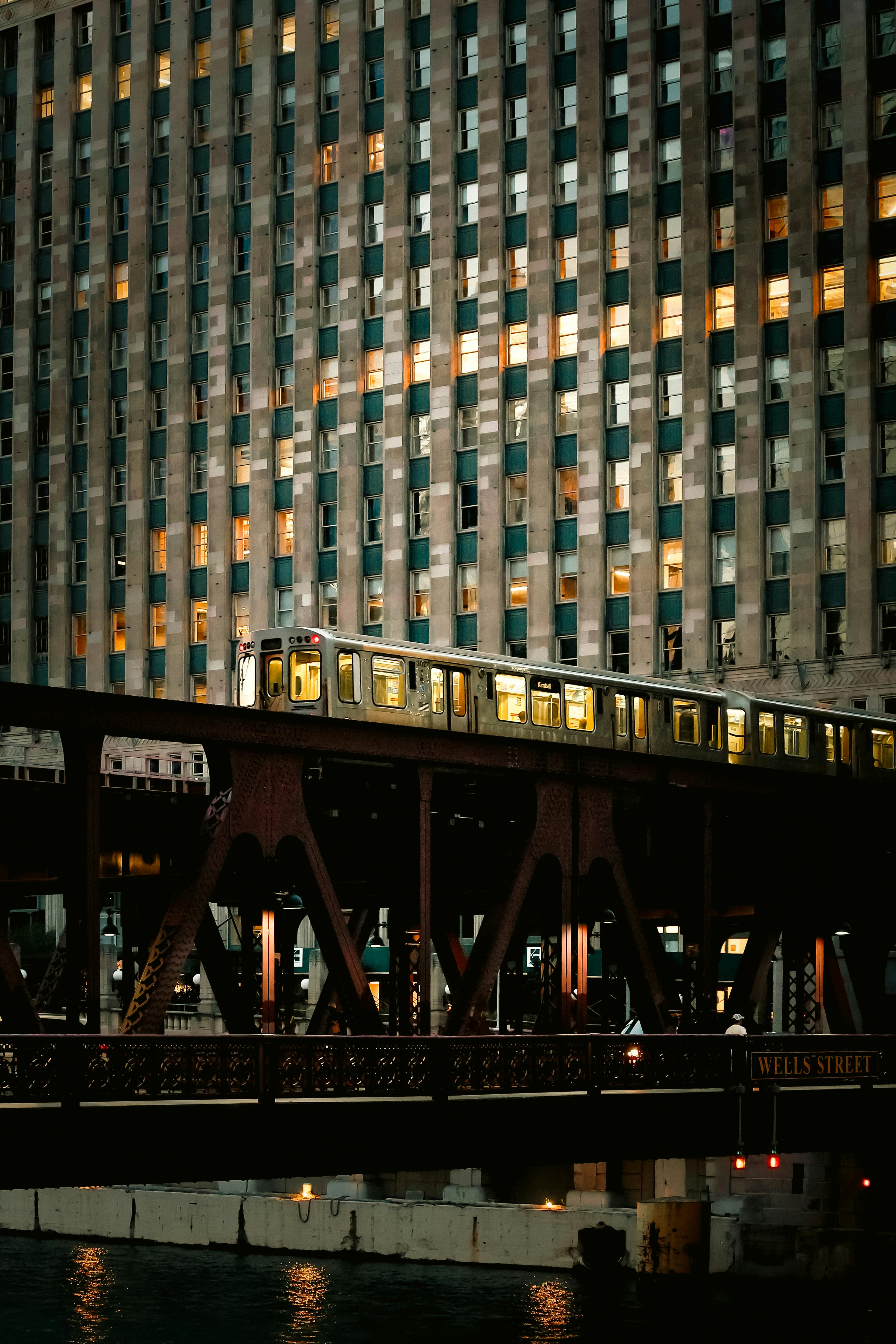 An elevated train crosses the Wells Street Bridge in Chicago at twilight, featuring city architecture.