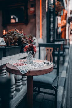 A quaint outdoor café setting featuring a wooden table with flowers and a blurred background.
