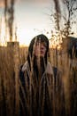 日落时分天色阴沉，一名身穿连帽衫的年轻人站在高高的草丛中，散发着沉思的气息