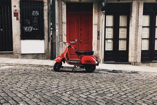 Free A charming red Vespa scooter parked on a cobblestone street in front of historic urban architecture. Stock Photo